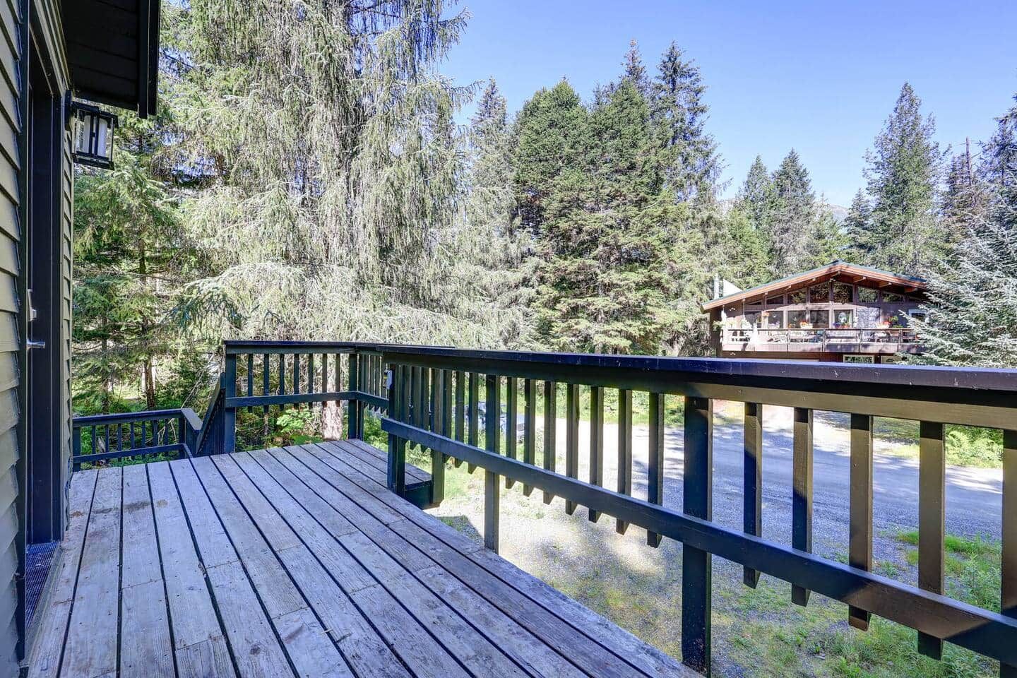 Um deck de madeira com guarda-corpo, com vista para uma área arborizada e um chalé.