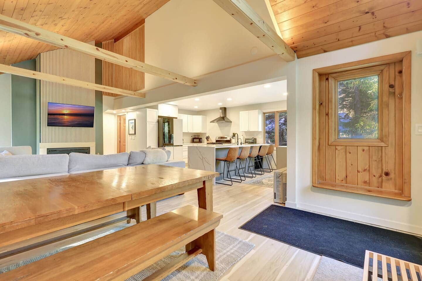 A modern interior with a wooden dining table, a sofa, and a kitchen area with bar seating.