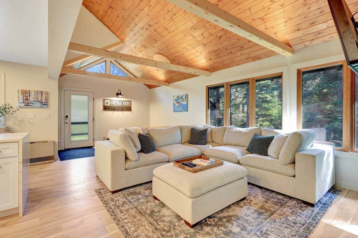 A spacious living room with a high ceiling and large windows, a sectional sofa, and a rug.