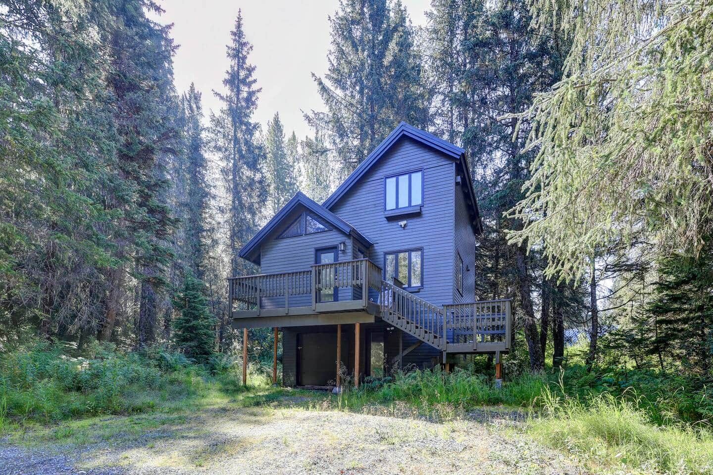 A two-story cabin with a balcony, surrounded by dense forest.