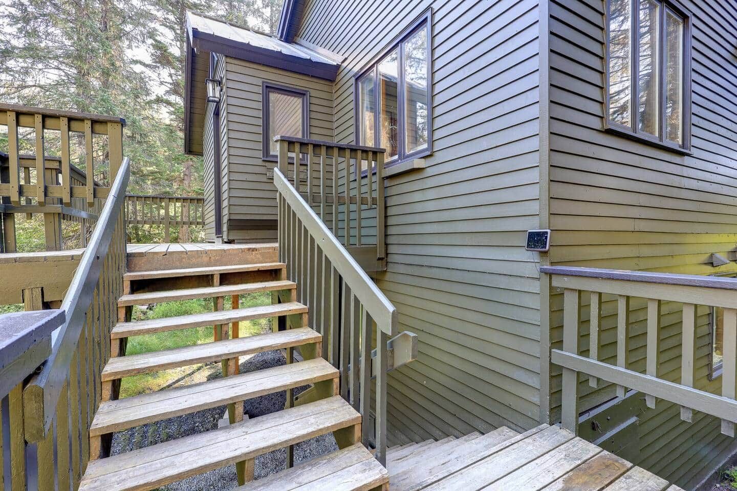 A wooden staircase leading to a house with a metal railing and a small window.