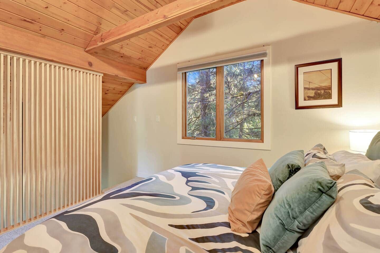 A bedroom with a bed, pillows, a window, and a framed picture on the wall.
