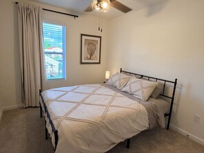Un dormitorio con cama, ventilador de techo, ventana con cortinas y una lámpara fijada a la pared.