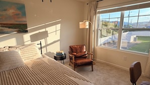 A bedroom with a large bed, a chair, a nightstand, a lamp, and a view of the outdoors. - Kingsport Time Capsule - 3 bedrooms near  Eastman and Holston Valley hospital (Kingsport)