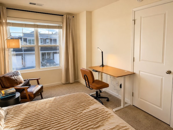 Habitación de hotel con cama, escritorio, silla, lámpara y vistas a edificios a través de la ventana.