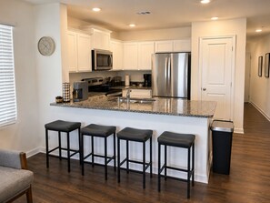 A modern kitchen with white cabinets, stainless steel appliances, a granite countertop, and four bar stools. - Kingsport Time Capsule - 3 bedrooms near  Eastman and Holston Valley hospital (Kingsport)