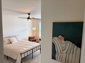 Un dormitorio con una cama, una silla, un ventilador de techo y un cuadro.