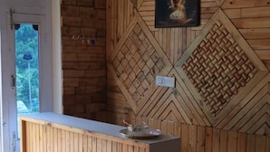 A reception desk with a wooden finish, a framed picture on the wall, and a door with a view of greenery outside.