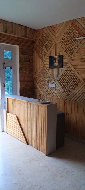 A reception desk with a wooden finish, a framed picture on the wall, and a door with a view of greenery outside.
