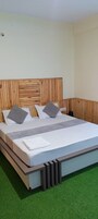 Uma cama de solteiro com cabeceira de madeira, roupa de cama branca e almofadas cinzas.