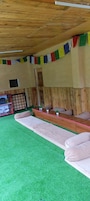 Una habitación con un largo banco de madera, césped artificial verde y una mesa roja con pequeñas macetas.