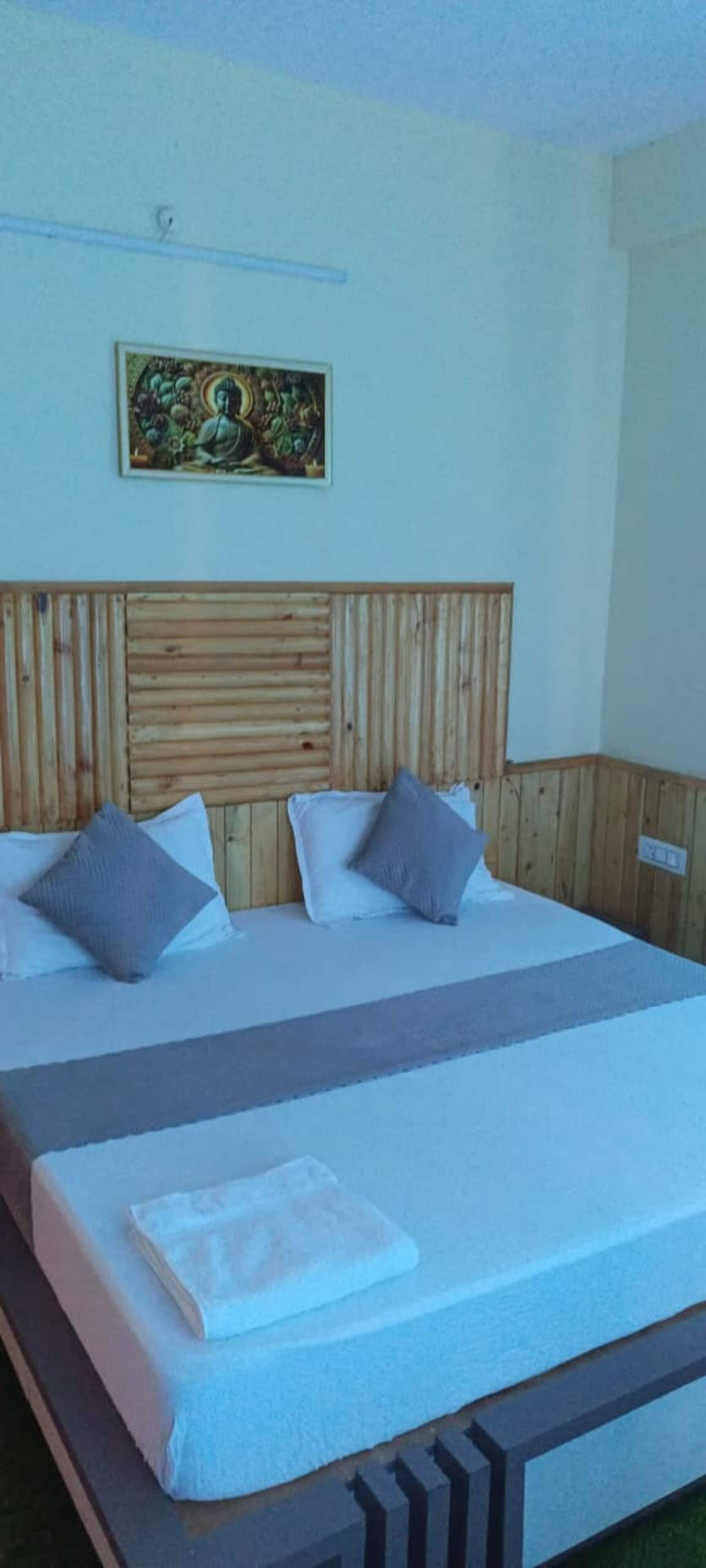 Una cama con cabecera de madera, dos almohadas y una toalla blanca doblada.