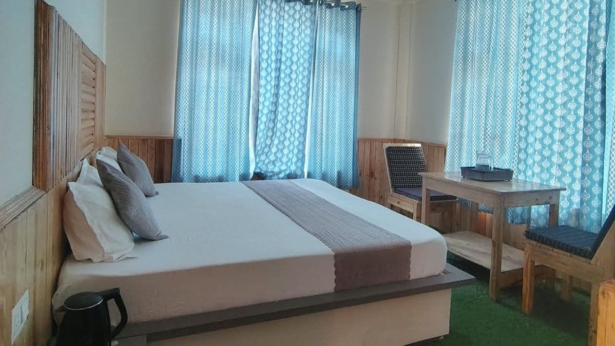 A hotel room with a bed, a small table, a chair, and curtains.