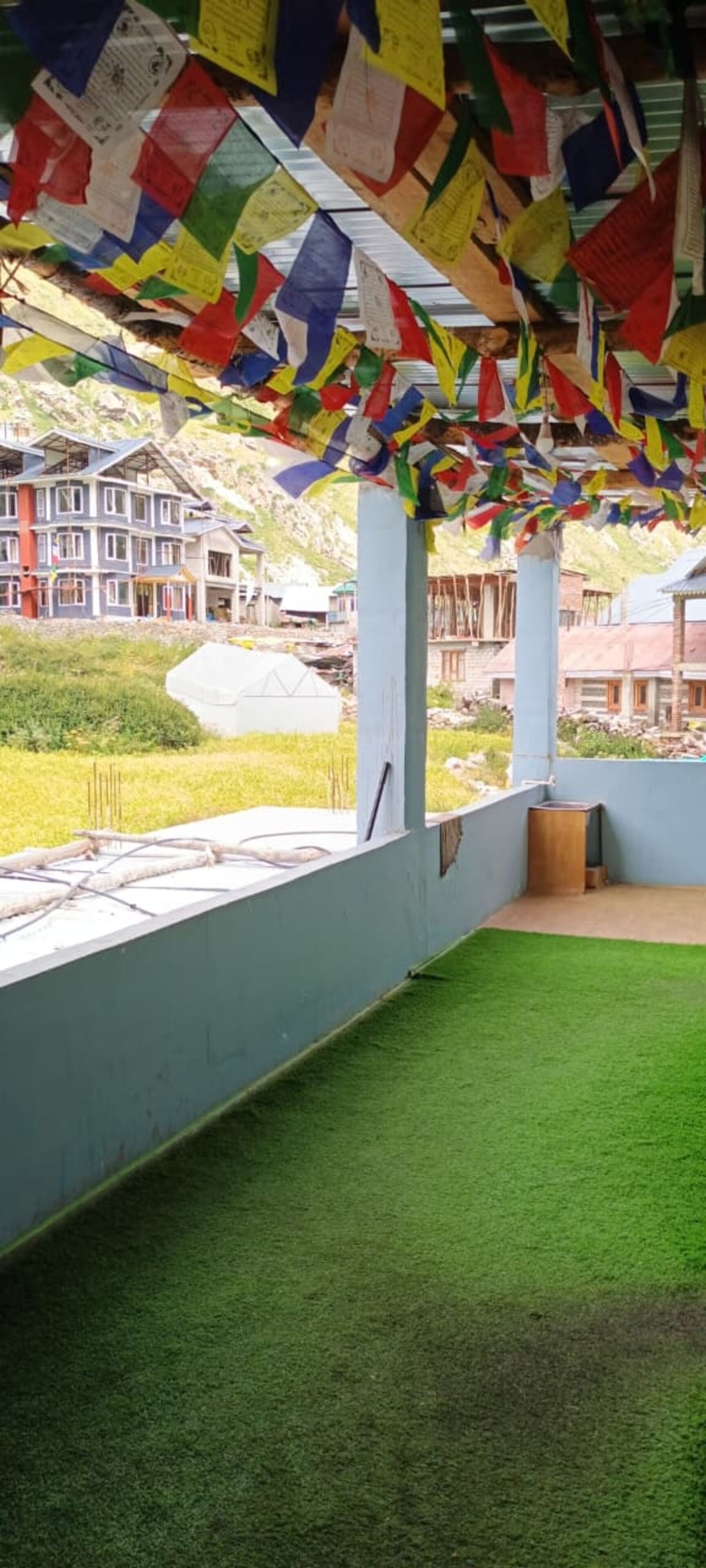 Una habitación con piso de césped artificial verde, pared blanca y ventana con vista a un edificio de múltiples ventanales.