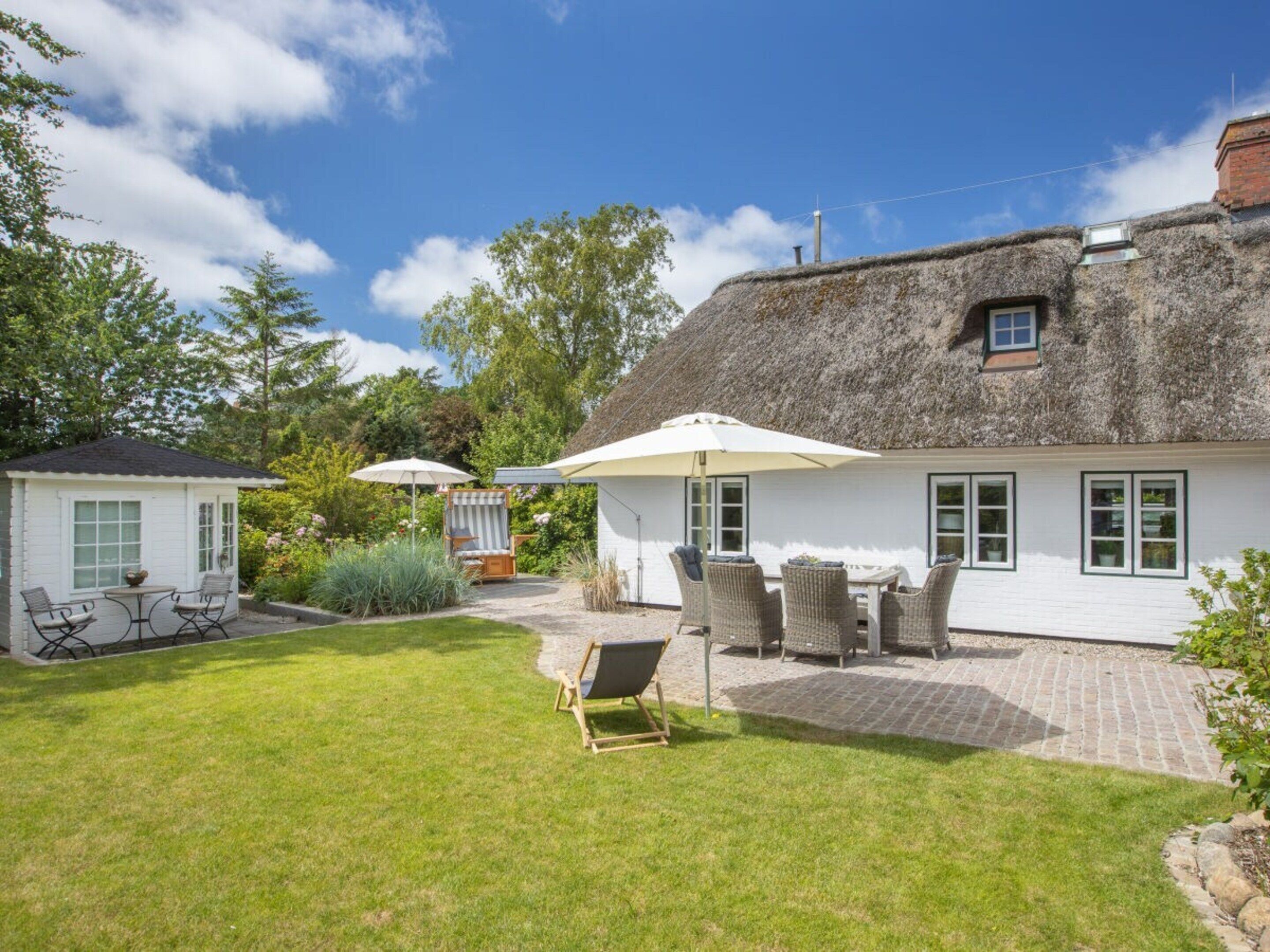Une maison avec un toit de chaume, une terrasse avec des meubles d’extérieur et un jardin bien entretenu.