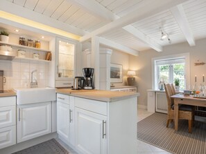 A modern kitchen with white cabinetry, a coffee maker, and a dining area with a table and chairs. - Reetkate Sandwehle (Kirchspiel Garding)