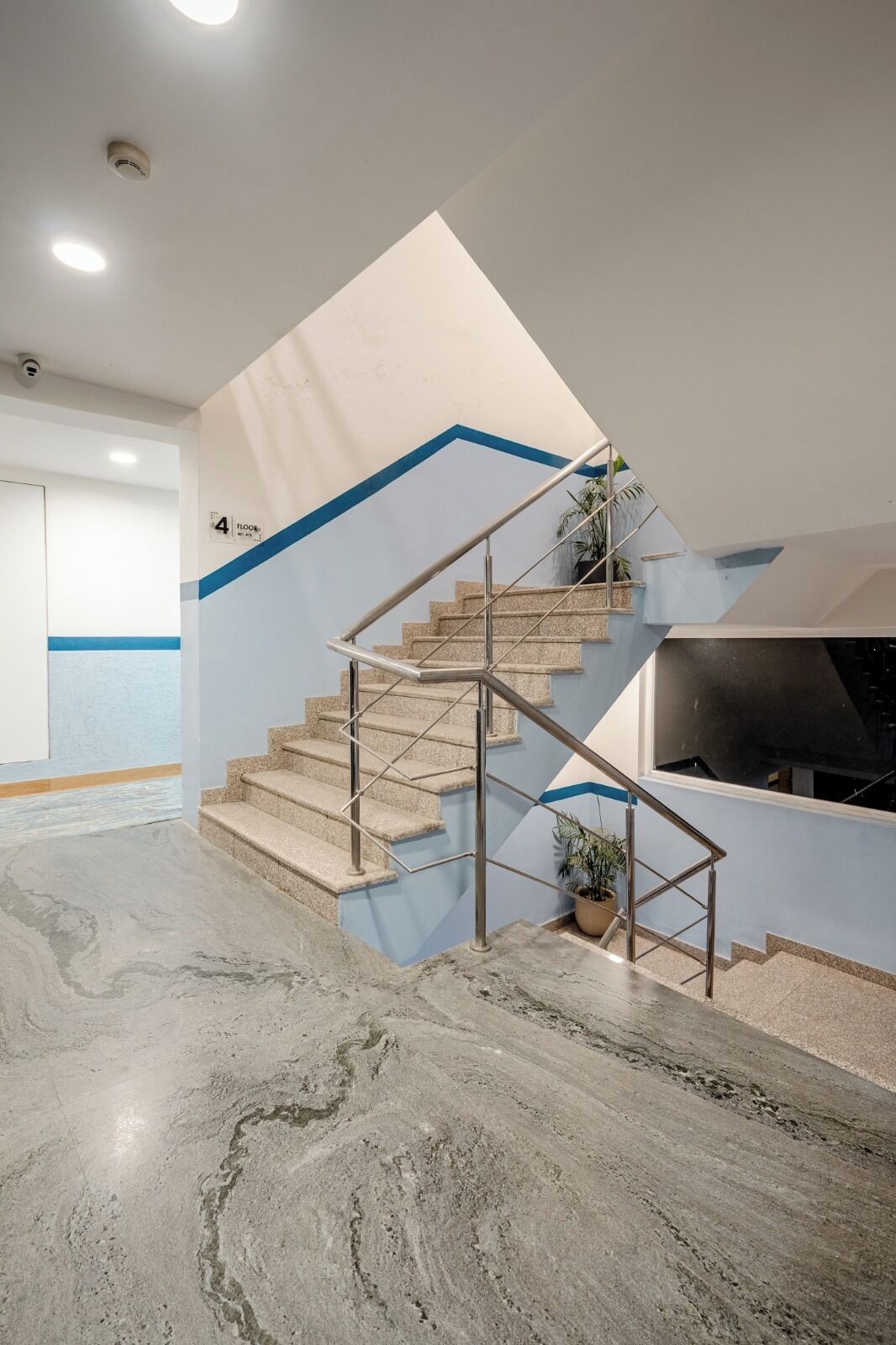 Una escalera moderna con barandales de metal, una planta en maceta y una pared de acento azul.