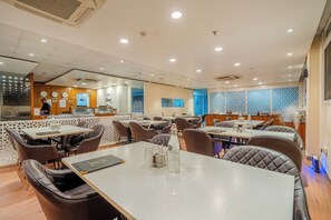 Een restaurant met meerdere tafels en stoelen, een toonbank en een decoratieve muur met geometrische patronen.