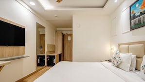 Et hotelværelse med en seng, et fjernsyn ophængt på væggen, et sengebord og et natbord.