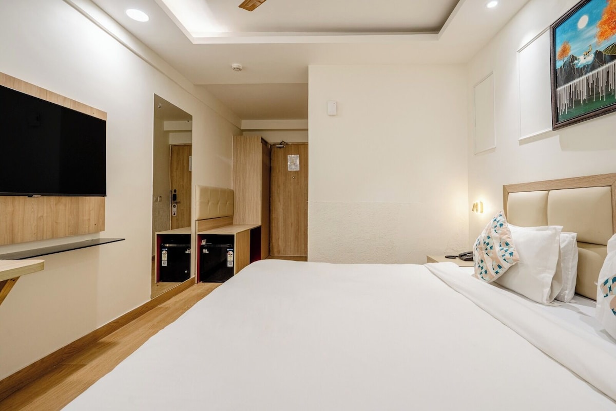 Een hotelkamer met een bed, een aan de muur bevestigde televisie, een nachtkastje en een bedtafel.