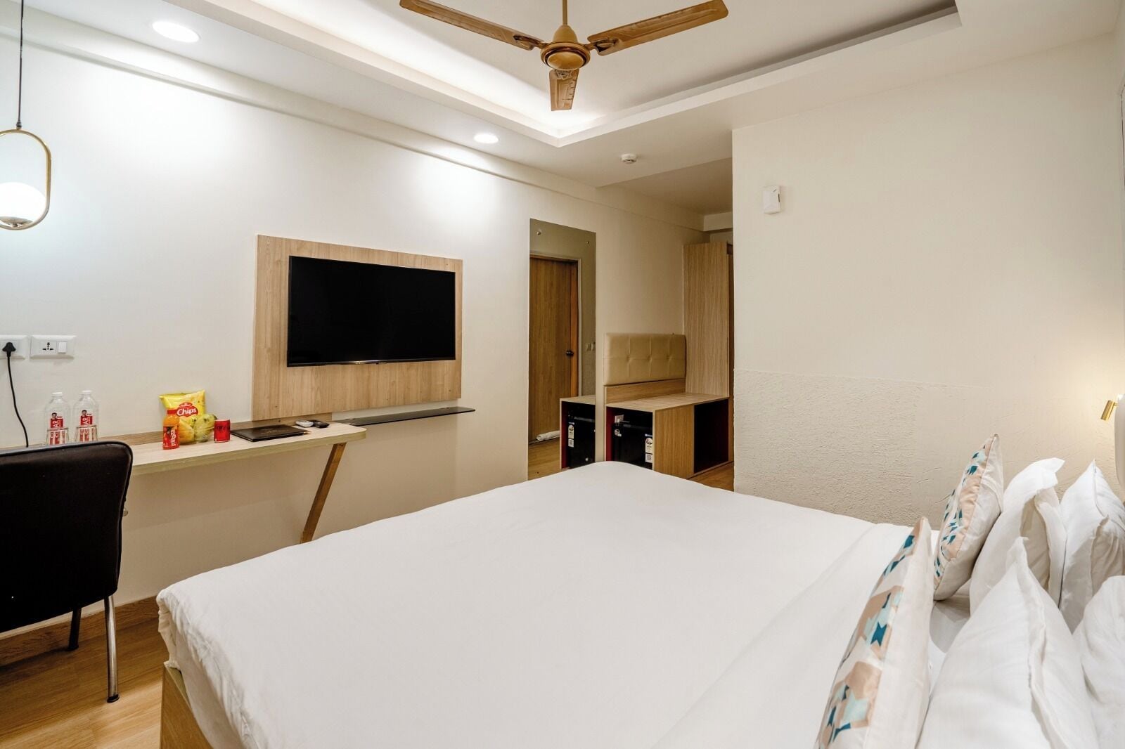 Habitación de hotel con una cama, un escritorio con televisor de pantalla plana, ventilador de techo y armario.
