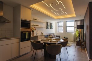 Una cuina moderna amb electrodomèstics integrats, una zona de menjador amb taula rodona i un espai de saló amb sofà i televisió.