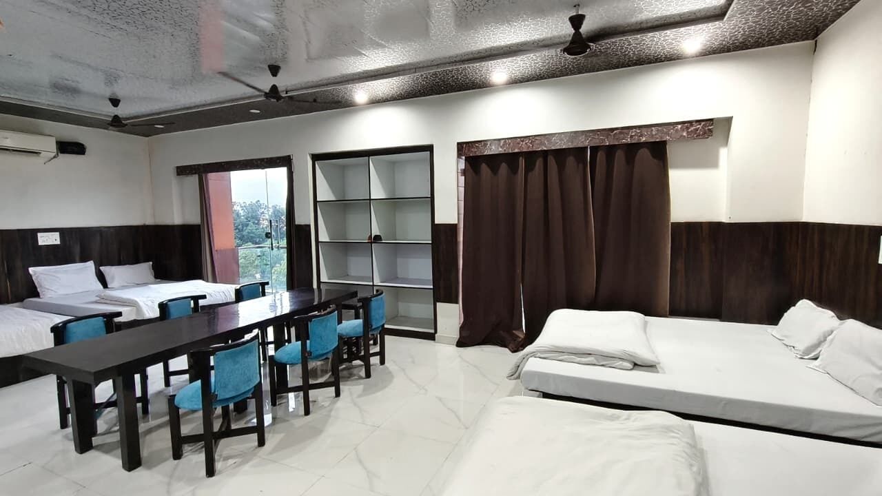 Una habitación de hotel con una cama, un escritorio con sillas, una estantería y una ventana con cortinas.