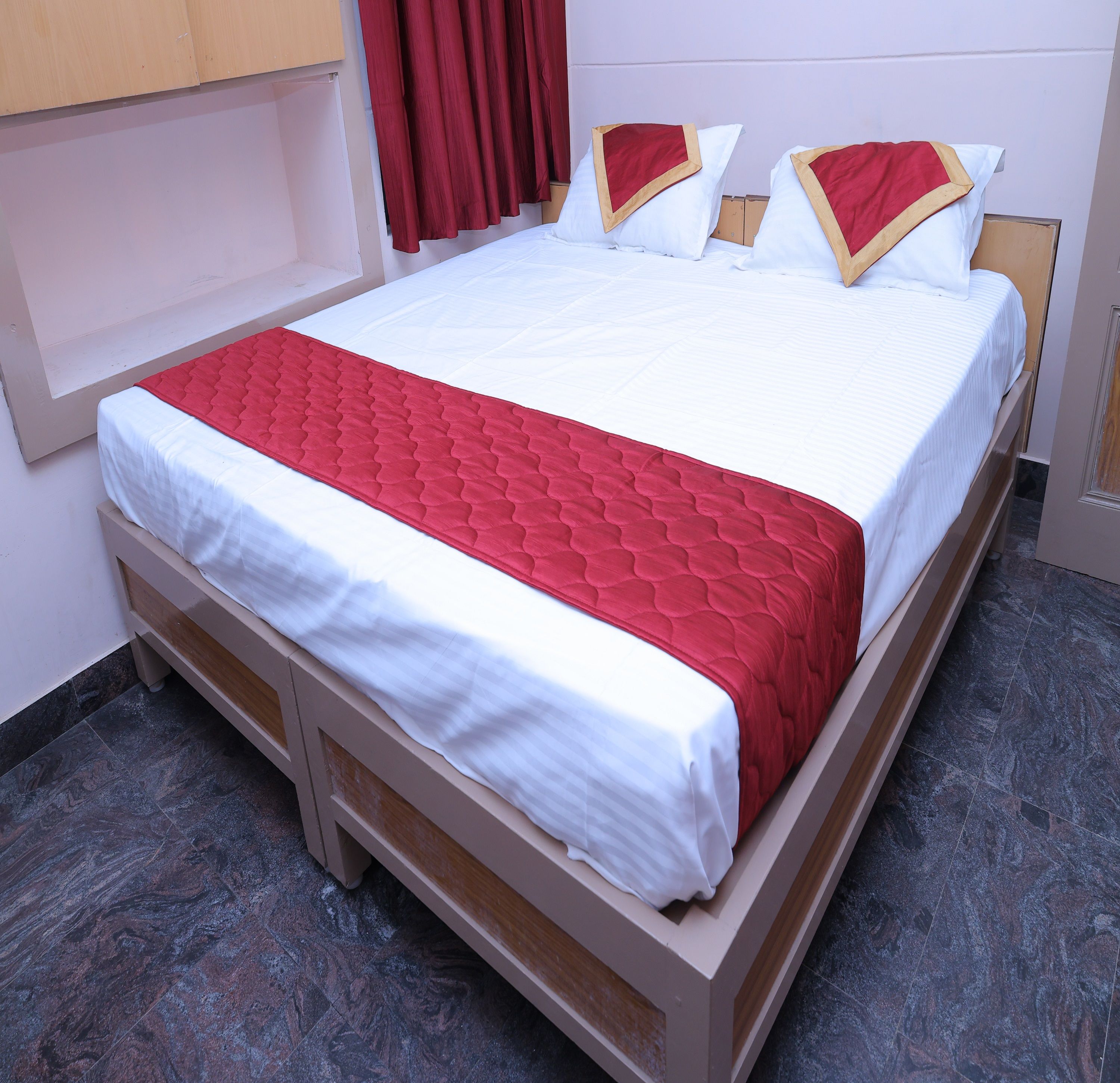Quarto de hotel padrão com uma cama, um edredom vermelho e branco, e uma cabeceira de madeira.
