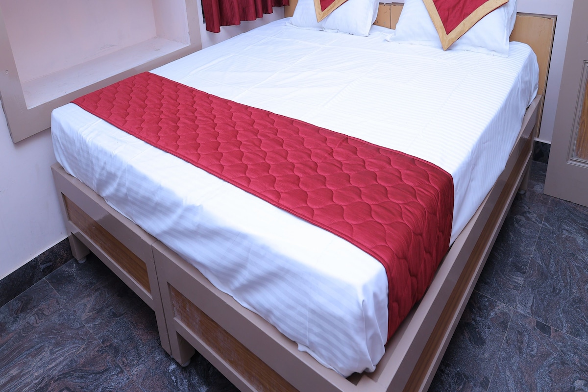 A standard hotel room with a bed, a red and white bedspread, and a wooden headboard.