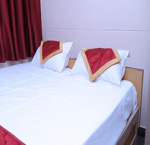A double bed with white bedding and red and gold decorative pillows.