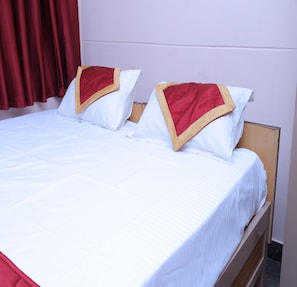 A double bed with white bedding and red pillows, a wooden headboard, and a red curtain in the background.