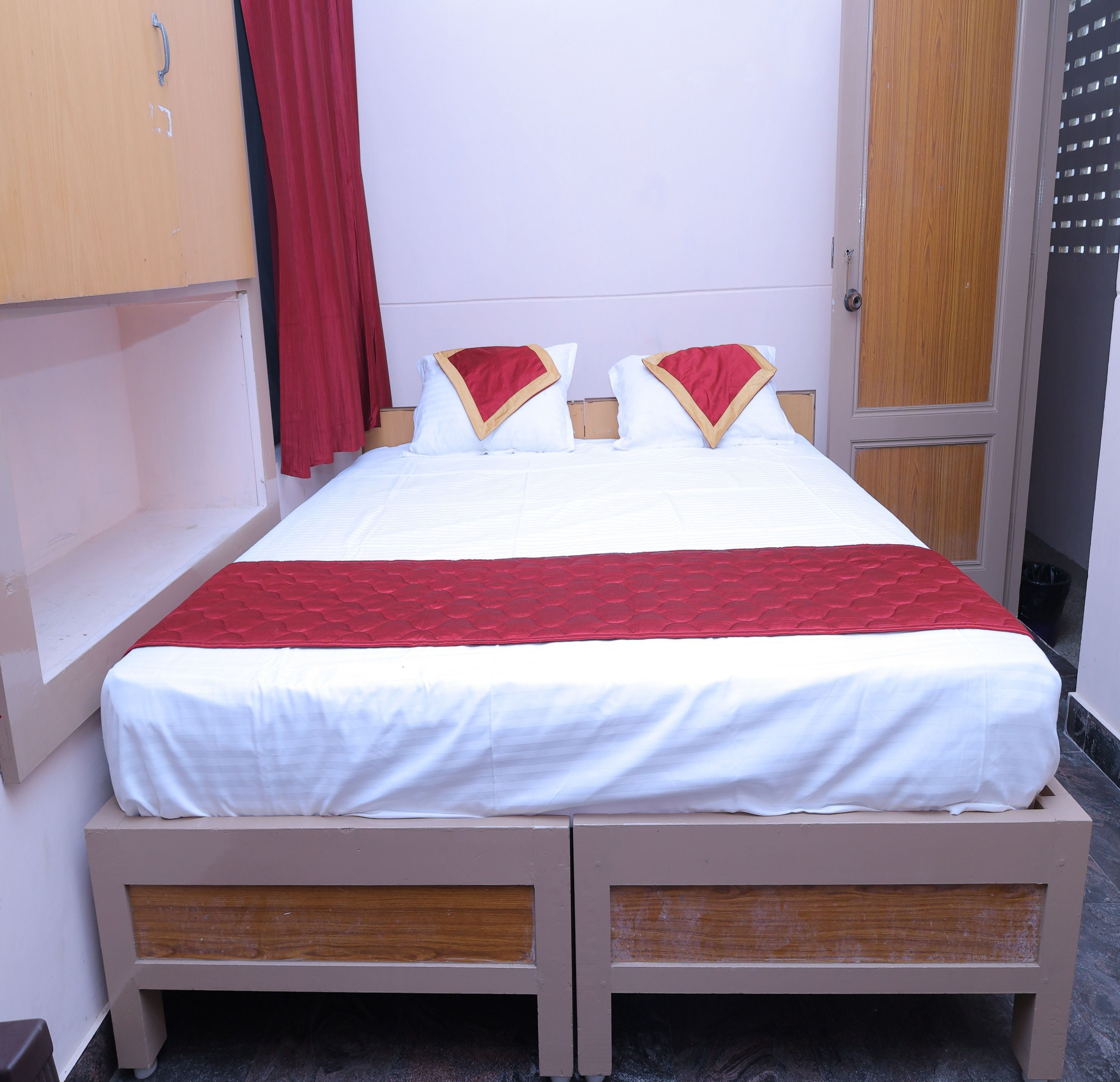 Habitación con cama individual, cabecera de madera, colcha roja y blanca, y cortina roja.