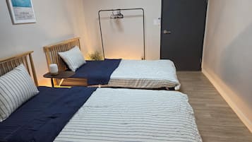 A room with two beds, a small table, a wall-mounted shelf, and a door.