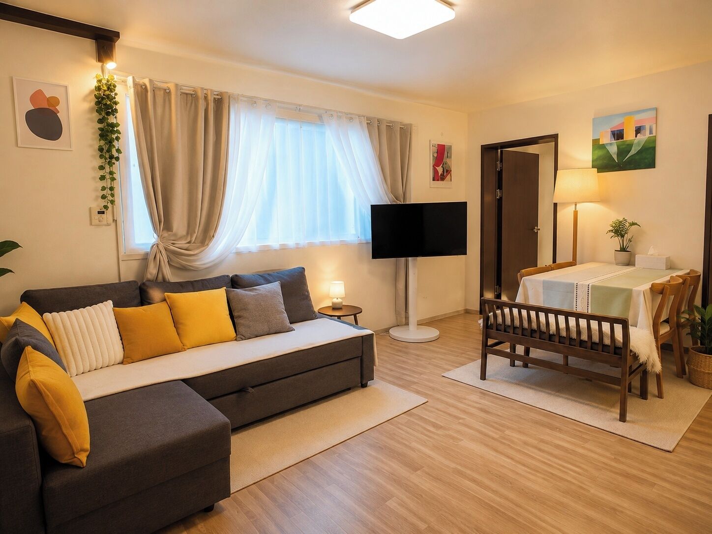 A modern living room with a sofa, a television, a dining table with chairs, and a small side table.