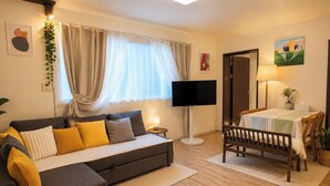 A modern living room with a sofa, a television, a dining table with chairs, and a small side table. - Lumi House Itaewon (Seoul)