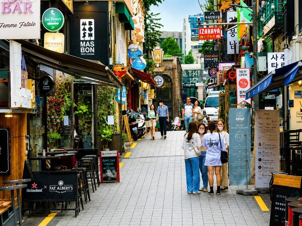 Una calle animada con diversos restaurantes y tiendas, incluyendo un letrero visible de Mas Bon y un letrero de Heineken.
