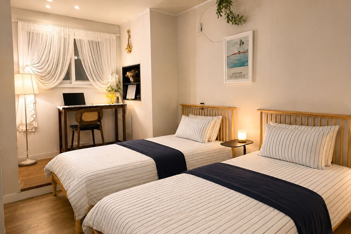 A hotel room with two beds, a desk, a chair, a lamp, and a framed picture on the wall.