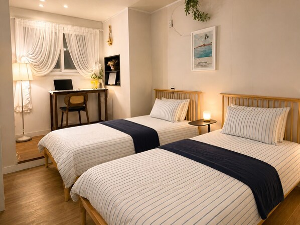 A hotel room with two beds, a desk, a chair, a lamp, and a framed picture on the wall.