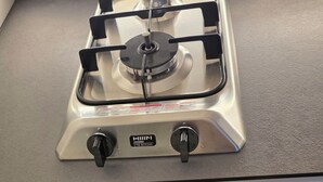 Una cocina con estufa a gas, un cajón con utensilios y una cuchara con mango de madera.