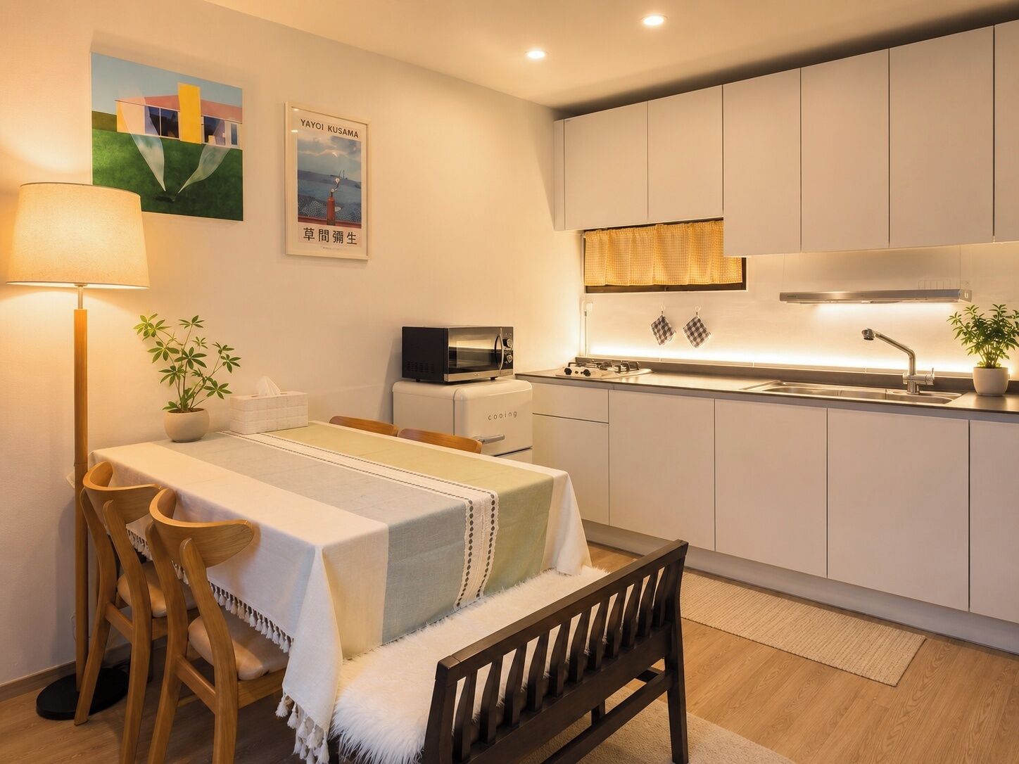 A compact kitchen with white cabinets, a microwave, and a sink. There's a dining table with chairs and a bench.