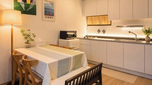 A compact kitchen with white cabinets, a microwave, and a sink. There's a dining table with chairs and a bench. - Lumi House Itaewon (Seoul)