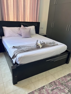 Een bed met een grijze deken en kussens, een zwart hoofdbord en een grijze kledingkast.