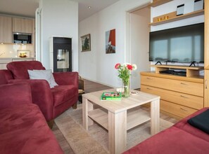 Uma sala de estar moderna com um sofá vermelho, uma mesa de centro de madeira e uma TV em um móvel de madeira.
