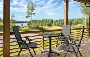 En träaltan med två stolar och ett bord, med utsikt över en sjö och en skog.
