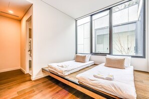 A room with two beds, a wooden floor, and large windows.