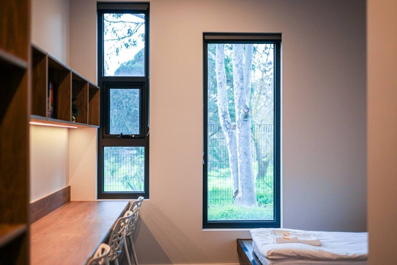 A room with a bed, a desk, and a window with a view of trees.