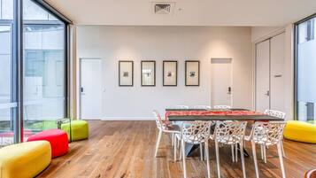 A modern meeting room with a wooden floor, white chairs, a long table, and colorful seating.