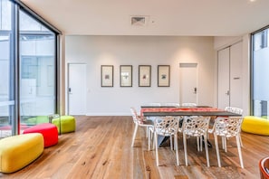 A modern meeting room with a wooden floor, white chairs, a long table, and colorful seating. - StayAU Bulleen Urban Hideaway 5BR (Bulleen)