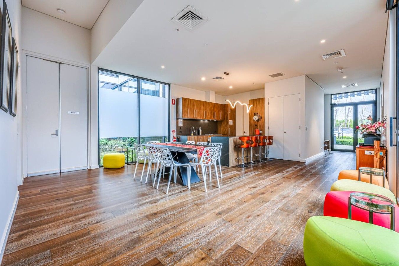 A modern kitchen with a dining area, wooden flooring, and large windows.