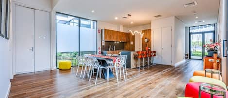 A modern kitchen with a dining area, wooden flooring, and large windows.